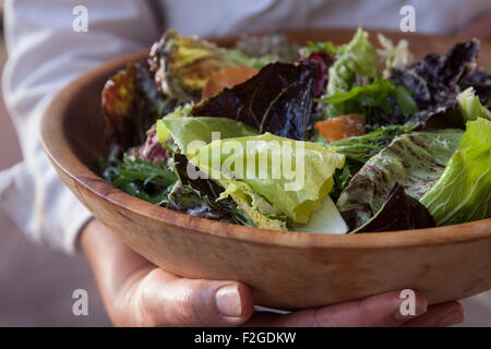 woman holds a wooden bowl with chicory salad against her body Stock Photo
