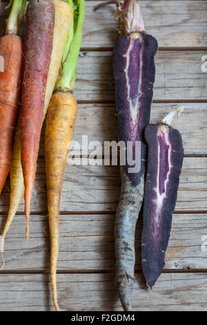 a bunch of rainbow carrots on rustic wood background, the purple carrot sliced vertically Stock Photo