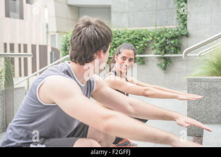 Couple of young handsome caucasian sportive man and woman doing squat in the city - focus on the woman looking and smiling at her friend - healthy, fitness, sportive concept Stock Photo