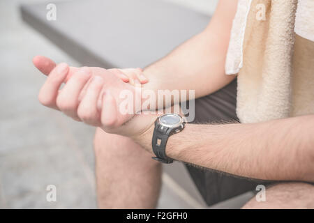 Close up on a sportive young handsome brown hair man checking his heart beats with his wristwatch, looking downward, with a towel around his neck - sportive, healthy, fitness concept Stock Photo