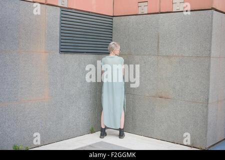 young handsome caucasian blonde italian designer view from back, posing in the city, wearing azure dress, overlooking left Stock Photo