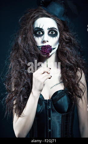Young woman in the image of a sad gothic freak clown holds withered flower