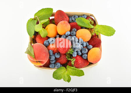 Mellow fresh summer strawberries, blueberries, apricots, peach and mint leaves in wooden basket isolated on white background, to Stock Photo