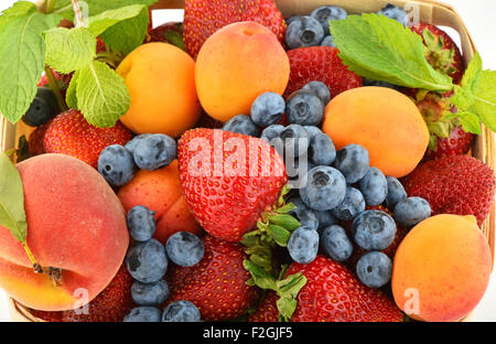 Mellow fresh summer strawberries, blueberries, apricots, peach and mint leaves in wooden basket isolated on white background, to Stock Photo