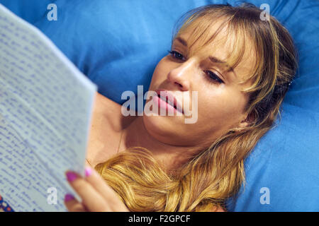 Young caucasian teenager receiving love letter from her boyfriend. The girl lays on bed and cries reading bad news. Stock Photo