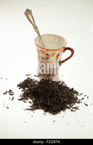 A pile of black tea with a silver teaspoon inside a small china cup.. Stock Photo