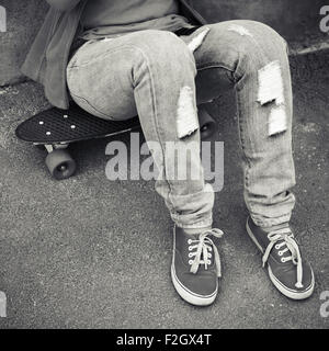 Teenager in jeans and gumshoes sits on a skateboard Stock Photo