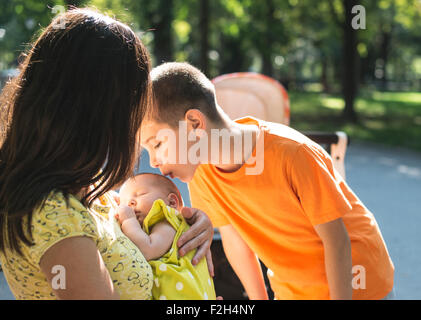 Women, brother and baby in a park. Child kissing baby Stock Photo