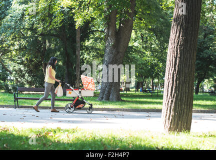 Mother walking in the park with baby buggy. Sunny day Stock Photo