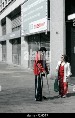 A disabled man on crutches and a woman talking in the street. Stock Photo