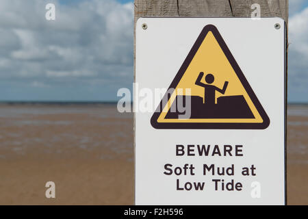 A warning sign reading Beware Soft Mud at Low Tide on a beach near to Prestayn in Wales. Stock Photo