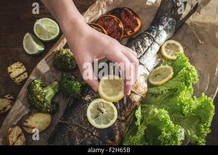 Roasted salmon and vegetables. Hand putting lemon on fish Stock Photo