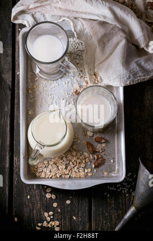 Set of non-dairy milk (rice milk, almond milk and oat milk) in glass cups and jug on old aluminum tray with rice grains, oat fla Stock Photo