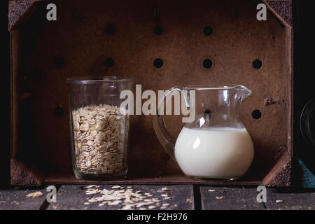 Glass jug of non-dairy oat milk and retro glass of oat flakes in wooden kitchen cabinet over old wooden table. Dark rustic style Stock Photo