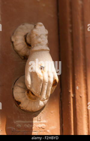 Old white rusty hand-shaped door knocker on brown wooden door closeup. Lefkara. Cyprus. Stock Photo