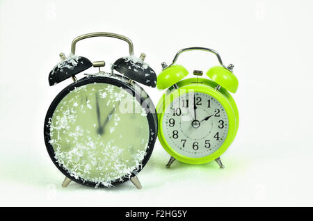 close up of   two retro alarm clocks, black and green, showing winter time and summer time, 1 am, 2 am, horizontal, snowy, icy Stock Photo