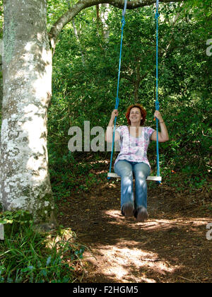 Forty year old woman playing on swing hanging from a tree, UK Stock Photo