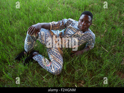 Benin, West Africa, Ganvié, fashionable young man in traditional beninese clothing resting in a field Stock Photo