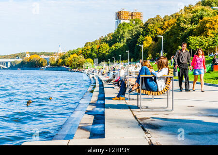 Moscow, Russia. Saturday, Sept. 19, 2015. Warm weekend. It is comfortable to be outdoors. The Moscow river and Andreevsky embankment. New benches installed along the embankment to have a rest by the river. Unidentified people sit on the benches and stroll along the embankment. Wild ducks in the water. The embankment was reconstructed and belongs to the Gorky park now. Tall building of the Presidium of the Russian Academy of Sciences (right). Credit:  Alex's Pictures/Alamy Live News Stock Photo