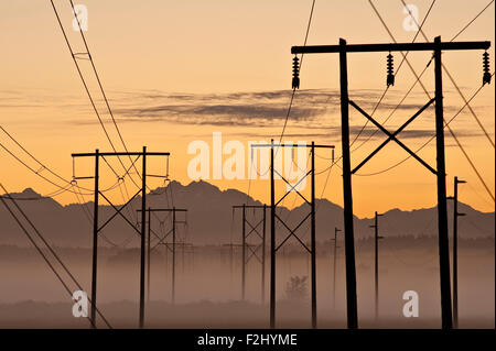 Sunrise with power lines and telephone wires stretching across valley floor Stock Photo