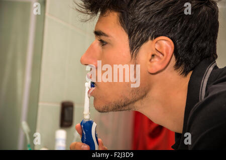 Headshot of attractive young man brushing teeth with toothbrush, looking at himself in mirror Stock Photo