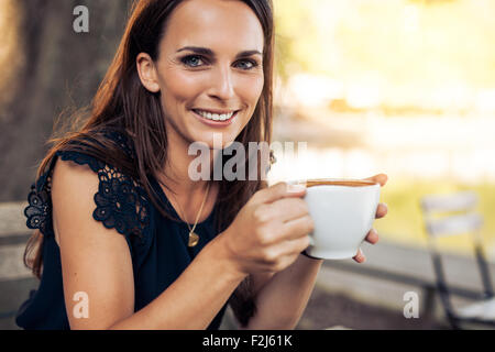 Portrait of smiling young woman with a cup of coffee in hand looking at camera while at cafe. Stock Photo