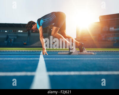 Male athlete on starting position at athletics running track. Runner practicing his sprint start in athletics stadium racetrack.