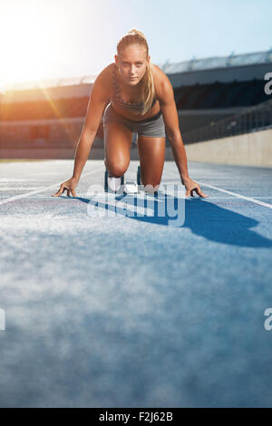 Young woman sprinter in the starter position on a race track at a sports stadium looking up at camera with determination. Runner Stock Photo