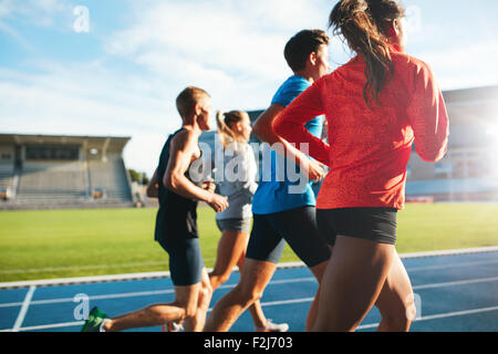 Rear view of young people running together on race track. Young athletes practicing a run on athletics stadium track. Stock Photo
