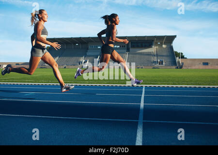 Athletes arrives at finish line on racetrack during training session. Young females competing in a track event. Running race pra Stock Photo