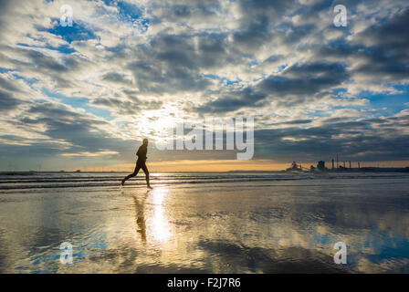 Jogger on beach with Redcar SSI steelworks blast furnace and coke ovens in distance.  Redcar, north east England Stock Photo