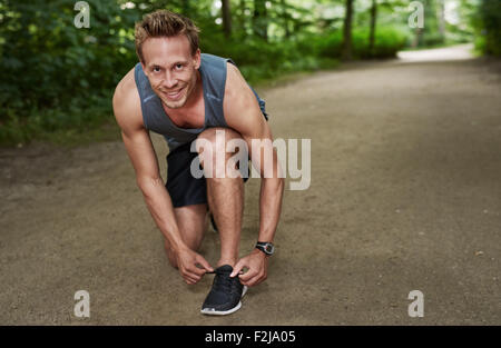 Healthy Muscular Man Smiling at the Camera While Fixing his Shoelace at the Park. Stock Photo