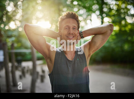 Half Body Shot of an Athletic Young Man at the Park Smiling at the Camera with Hands Behind his Head. Stock Photo