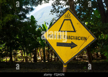 A crude sign directing towards a volcano evacuation route on the Island of Ometepe in Lake Nicaragua with a volcano in the back Stock Photo