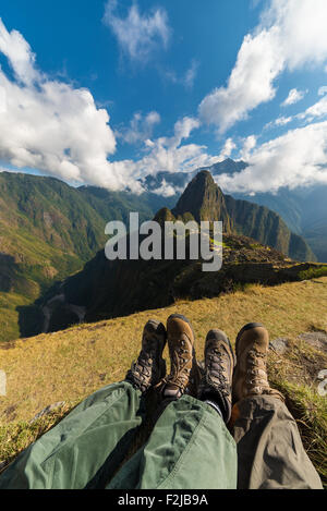 Wide angle view on Machu Picchu from the terraces above. Foots and hiking boots in the foreground. Blue sky with scenic clouds, Stock Photo