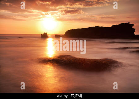 Stunning sunset on the rocky coastline of Bali, Indonesia. Silhouetted sea stacks help create a surreal image with added long exposure photo effects Stock Photo