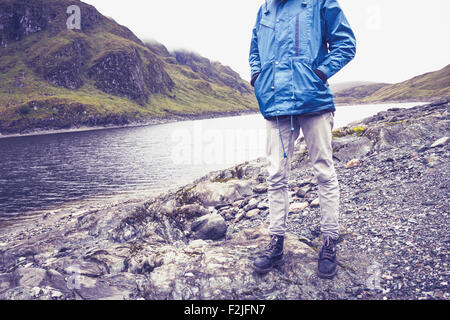 Young hiker standing by lake in mountains Stock Photo