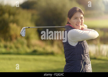 Smiling friendly young woman golfer looking at the camera after following through with her club after the shot, close up view of