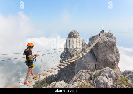 Young woman crossing the chasm on the rope bridge Stock Photo