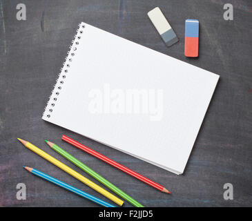 Blank notepad and colorful pencils on blackboard background. Top view with copy space Stock Photo