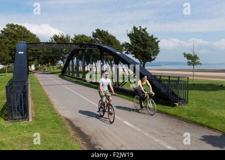 Cyclists cycle in a cycle lane along the Swansea beach promenade in Swansea, South Wales. Stock Photo