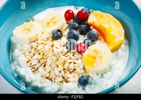 Healthy breakfast. Granulated cottage cheese plus oat flakes, banana, blueberries, red currant, peach and honey. Stock Photo