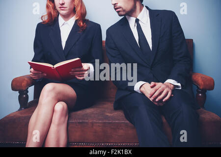 Young businesswoman and businessman reading a book on a sofa Stock Photo