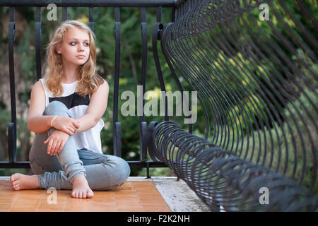 Beautiful blond Caucasian girl sits on balcony, outdoor summer portrait Stock Photo