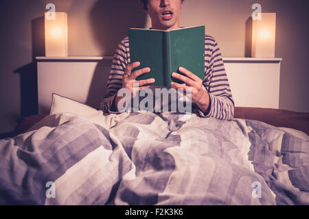 Young man reading book in bed at night Stock Photo
