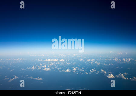 Aerial View Of Blue Sky And Clouds From Plane Window Over Mexico City Mexico / MEXICO CITY, Mexico — An aerial view from a plane window captures a vast expanse of blue sky and scattered white clouds. The aircraft is flying over Mexico, en route towards Mexico City, the nation's capital and largest urban center. The horizon line separates the deep blue upper sky from the lighter, hazy atmosphere below, where numerous small clouds are visible. This perspective offers a typical view from a high altitude flight. Stock Photo
