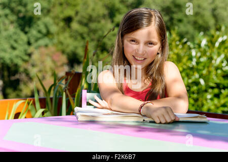 a little girl reads a book on the garden table Stock Photo