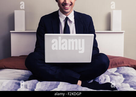 Young businessman sitting on bed and using laptop Stock Photo
