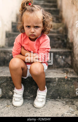 Portrait of little girl sitting on steps pouting mouth Stock Photo