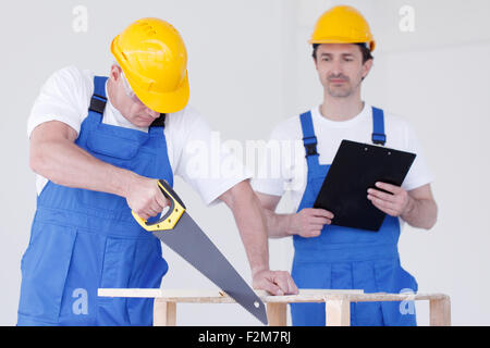 Two workmen in protective workwear with saw and folder Stock Photo
